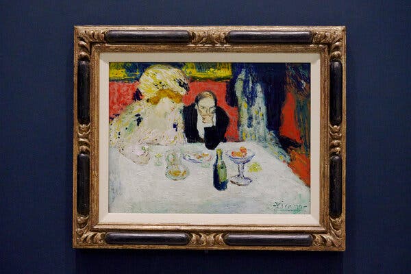 A man and woman at a table. The woman is dressed lavishly with a huge hat; the man looks a bit glum, his chin resting on his hand.